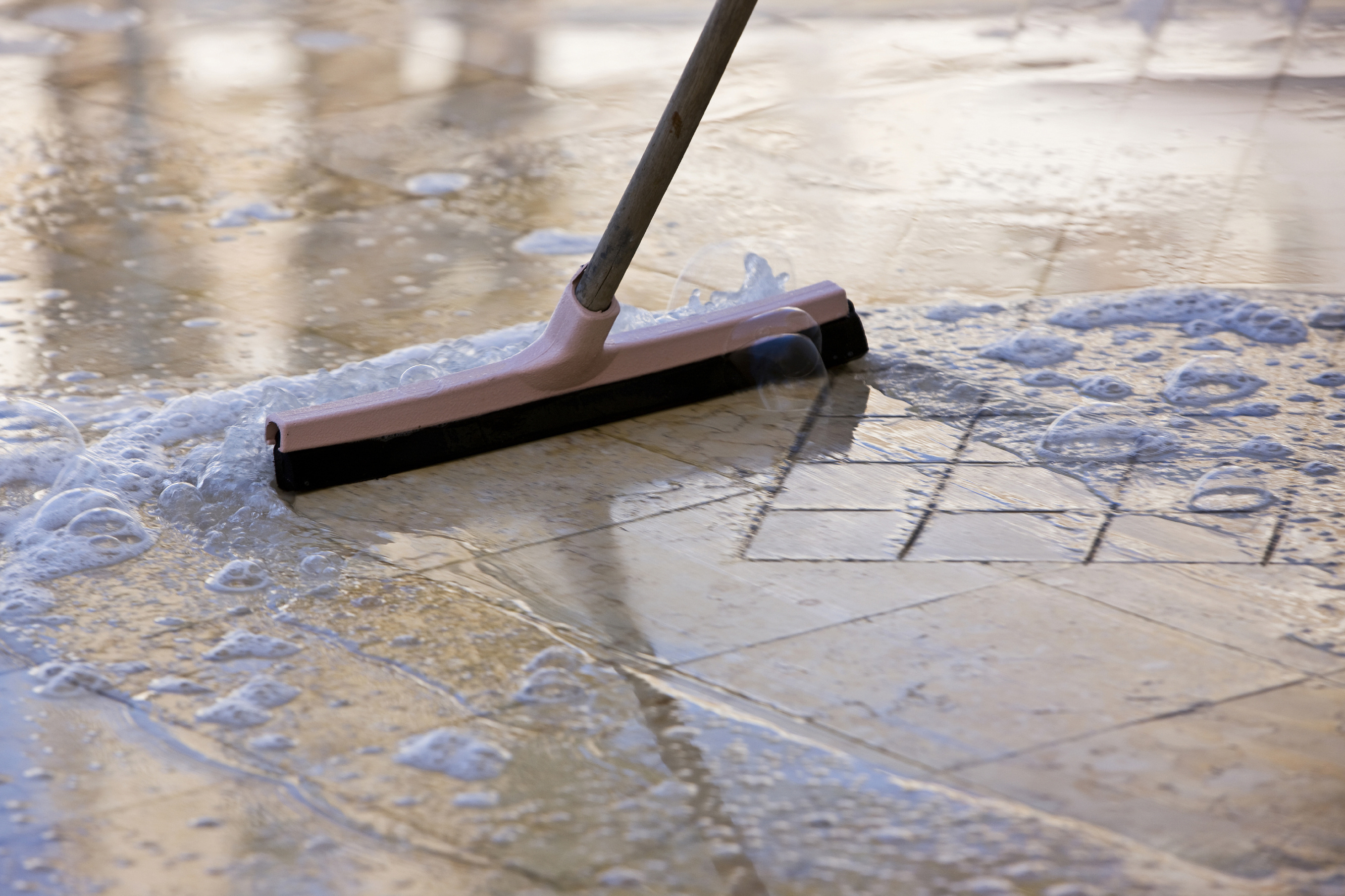 Soapy water being pushed across a floor with a wet broom.